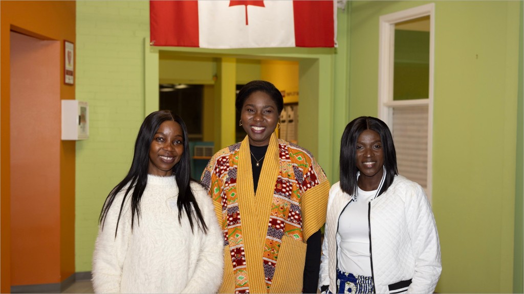 Three smiling newcomers standing together under a Canadian flag.