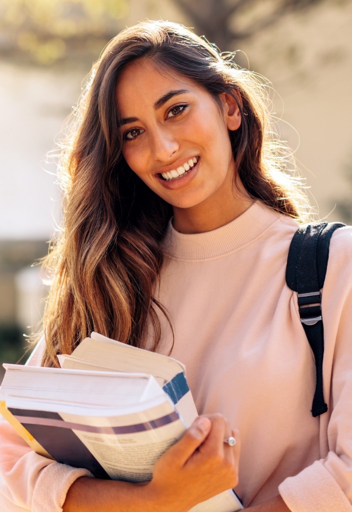 A smiling woman holding a stack of books