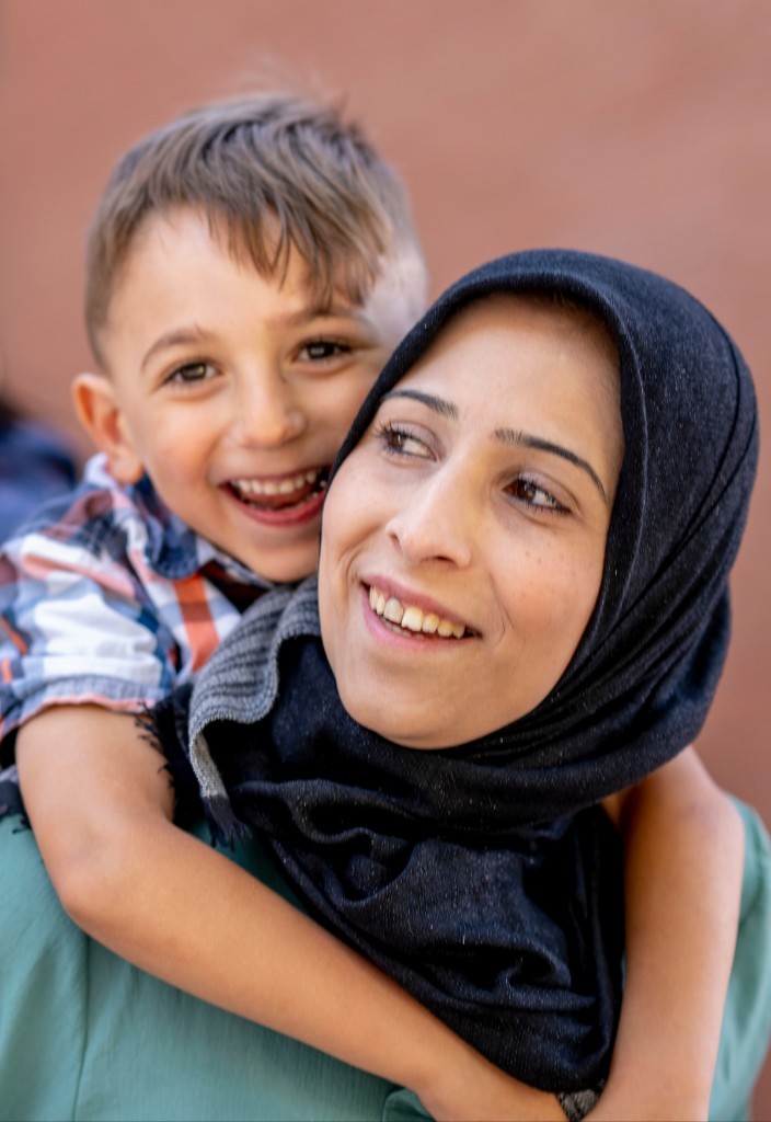 A smiling woman with a young child on her back